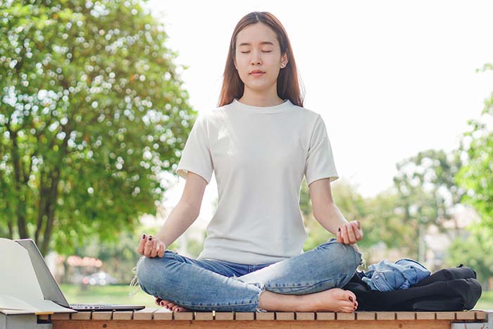 An Asian woman in a yoga position meditating in a park
