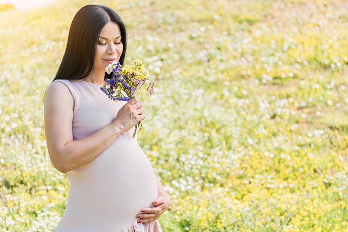 A pregnant woman holding her belly and smelling a bouquet of flowers