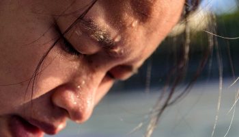 A close-up photo of an Asian woman looking down with sweat on her face