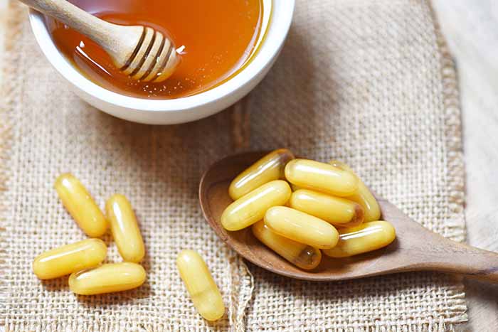 Royal jelly capsules in a wooden spoon alongside a bowl of honey