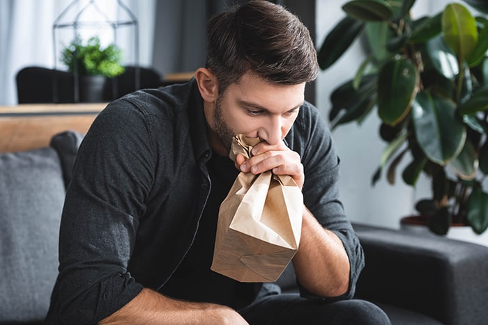 A man experiencing a panic attack sits down and breathes in a paper bag