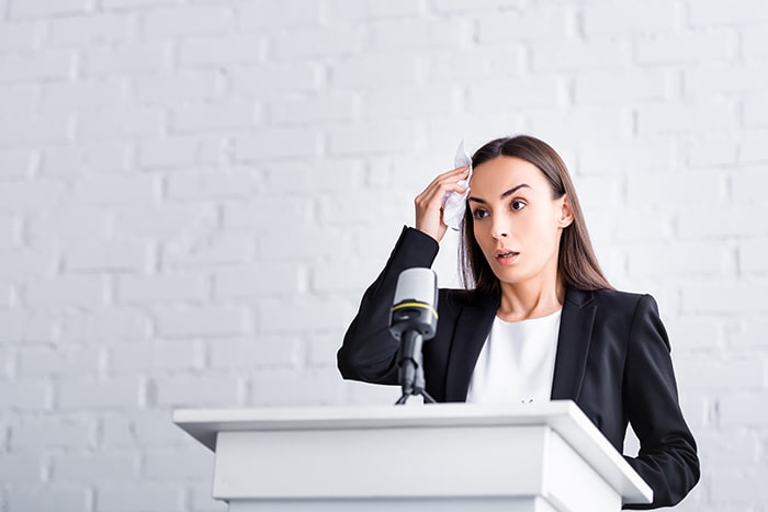 A woman suffering from glossophobia looks worried while standing on a podium