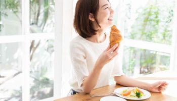 A woman eats a croissant and salad for lunch