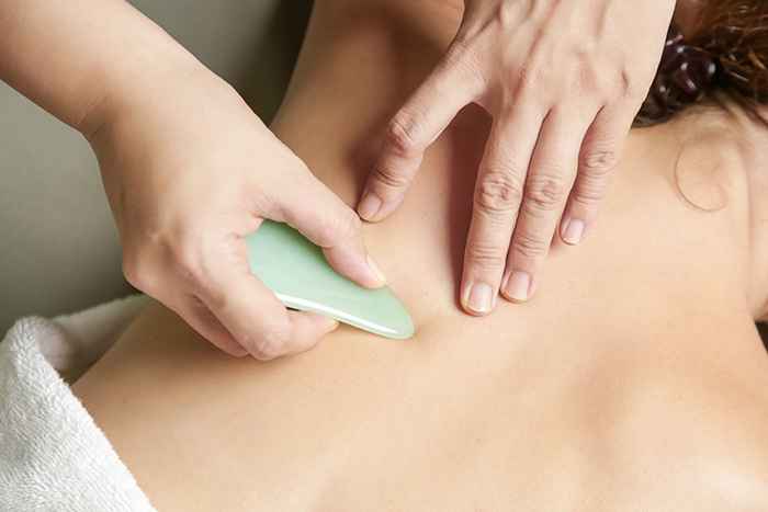 A jade stone gua sha being pressed into a woman’s shoulder
