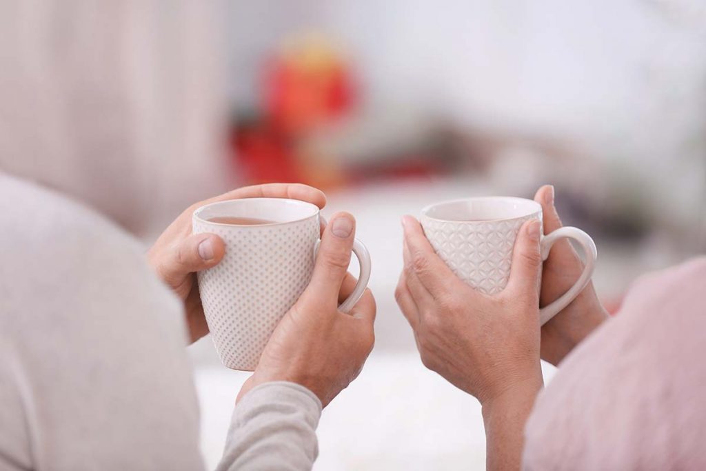 A pair of male and female hands holding white mugs