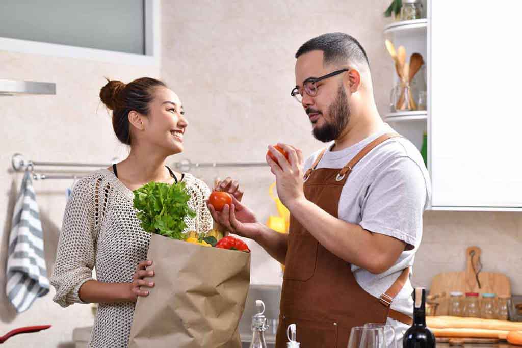 A young Asian couple having a light conversation in the kitchen while holding fresh produce
