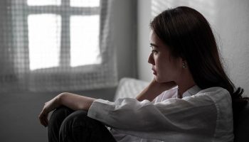 A woman sitting against a wall as she stares into the distance with a gloomy look on her face