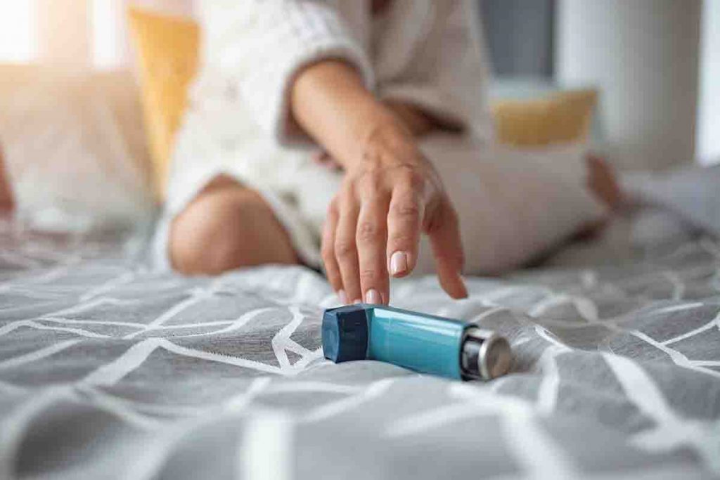 A woman in bed reaching for her asthma inhaler