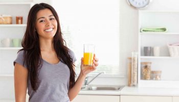 An Asian woman holding a glass of orange juice in the kitchen