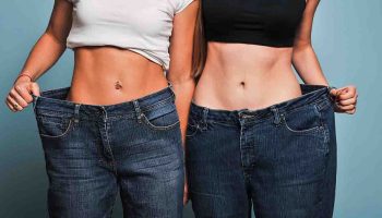Two women stand next to each other and pull the waistband of their oversized jeans