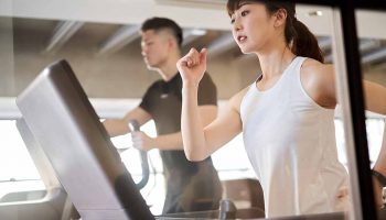 A sporty woman running on a treadmill beside a man who is also exercising with a machine