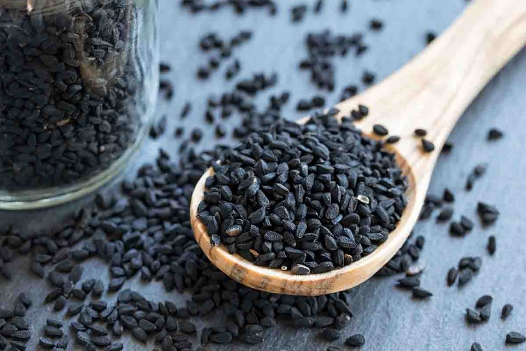 A spoonful of black cumin seeds displayed on a wooden table