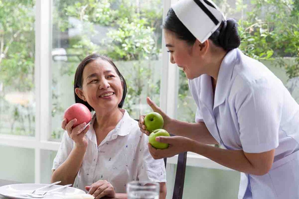 A nurse offering two green apples to an elderly woman