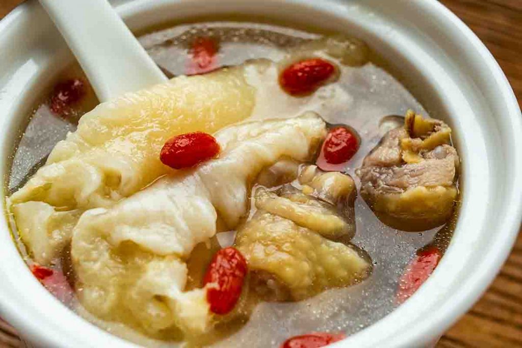 A bowl of herbal soup that contains chicken, fish maw and goji berries