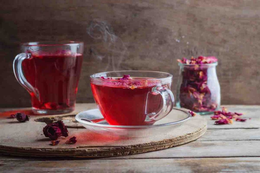 Two cups of rose tea and dried rosebuds placed on a glass