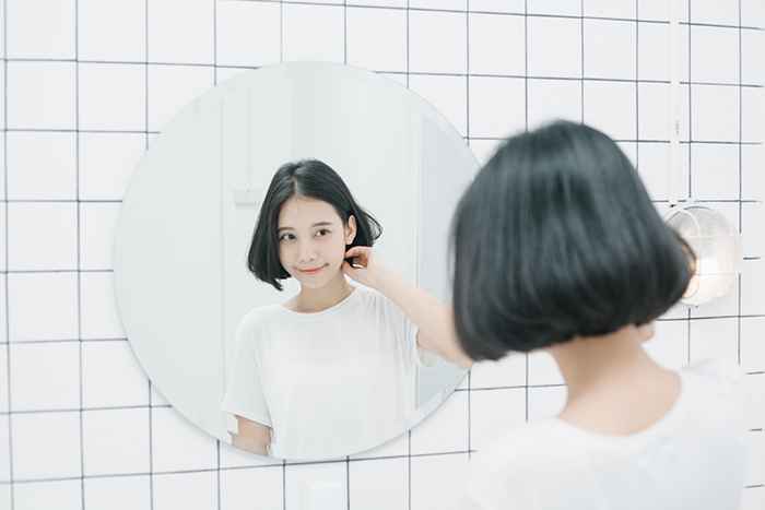 A young girl with her back facing the camera looking happily at her reflection in a mirror in front of her
