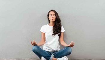 Woman in casual wear sitting with eyes closed and legs crossed while meditating