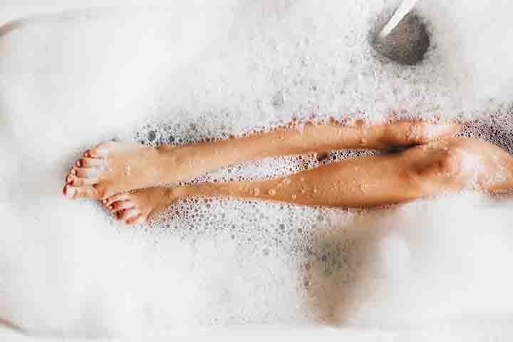 A top-down shot of a woman’s legs as she’s immersed in bubble bath
