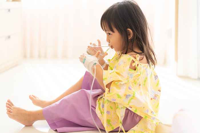 Toddler sitting in hospital bed drinking a glass of water