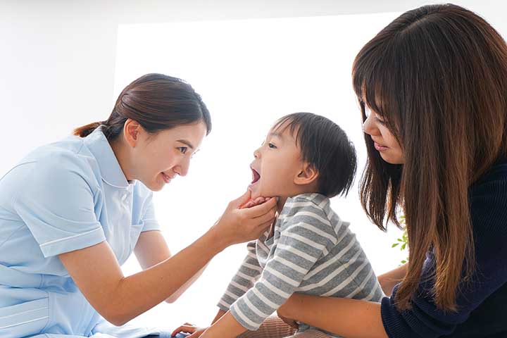 Doctor checking a boy’s mouth while his mother comforts him
