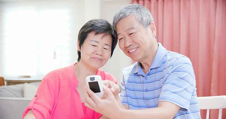 Elderly Asian man and woman holding a glucometer in hand and looking at the reading
