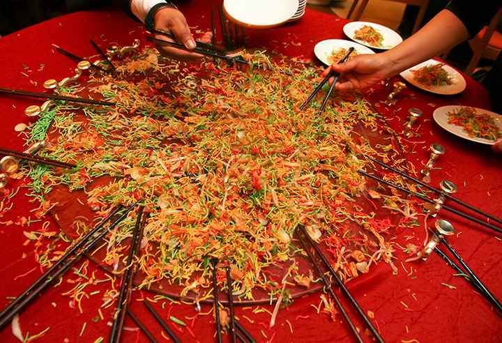 People tossing yee sang that’s served on a turntable using giant chopsticks