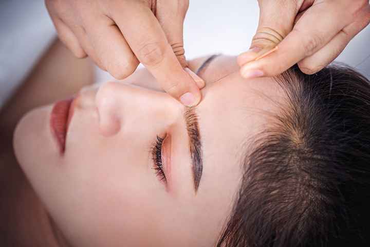 A close-up of a woman's face with an acupuncture needle being inserted into the skin between her brows.