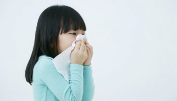 Sick girl sneezing into a tissue