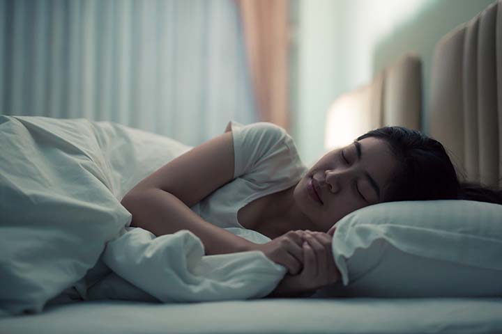 Woman sleeping on her bed in a dark lit room.