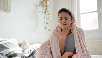 Woman with throat pain sitting up on the edge of the bed.