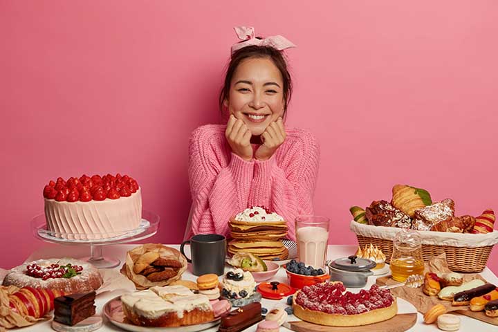 Girl smiles gleefully as she sits at a table of desserts and pastries.
