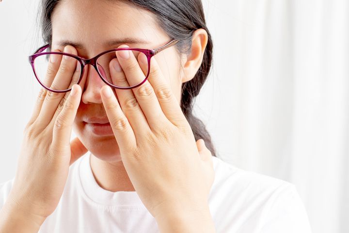 A woman wearing glasses and massaging her eyes