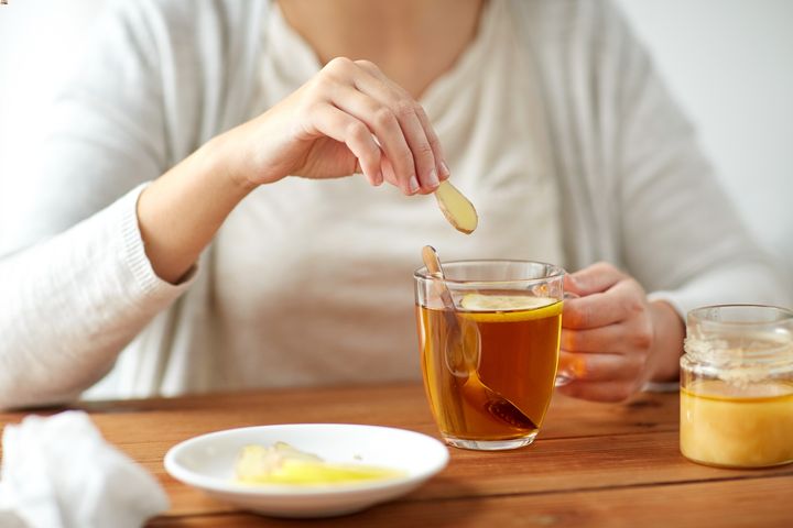 A woman putting a piece of ginger into a cup of tea