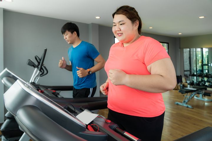 An obese woman is working out on a treadmill with a man to help her lose weight