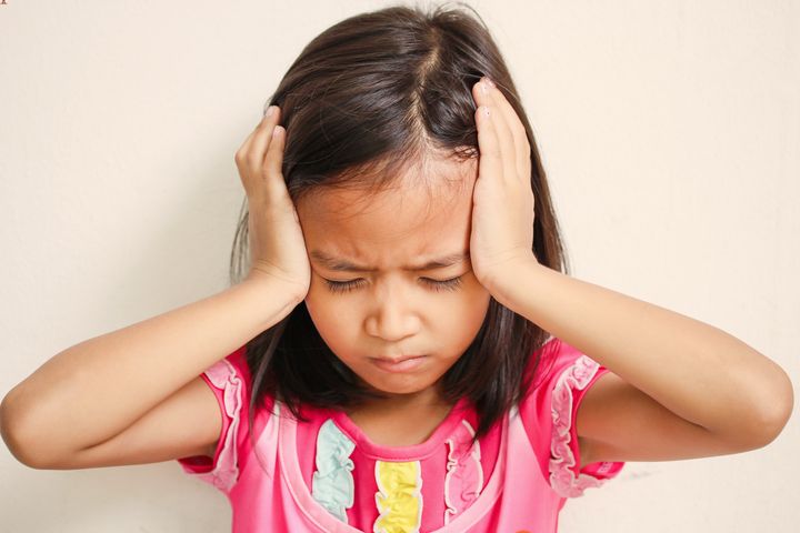 A girl holding the sides of her head with both hands while closing her eyes