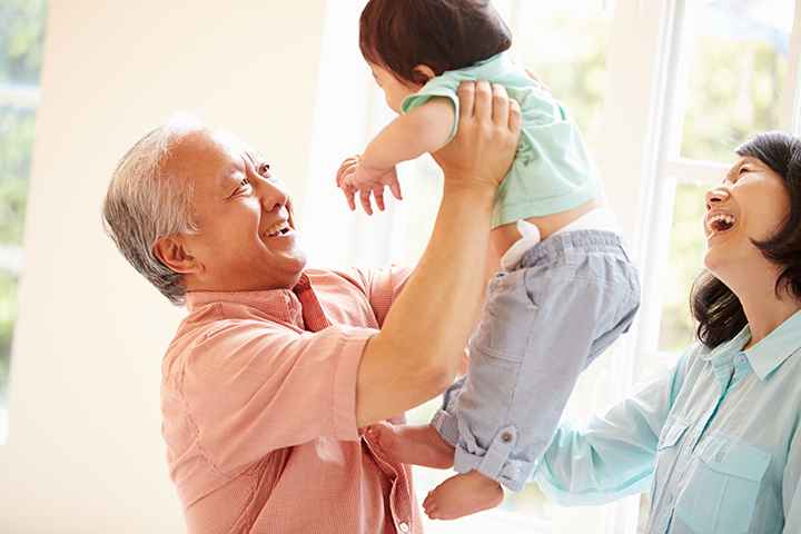 Elderly man lifting a toddler in the air as an elderly woman looks on