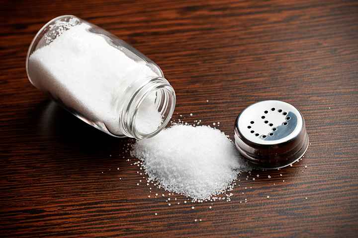 Salt spilling out of glass shaker and onto the table