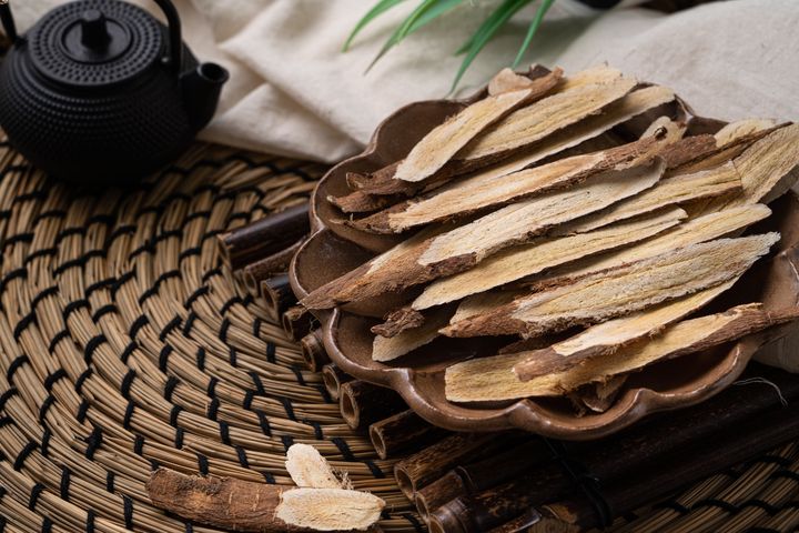 Dried and sliced astragalus roots in a decorative wooden bowl next to a teapot