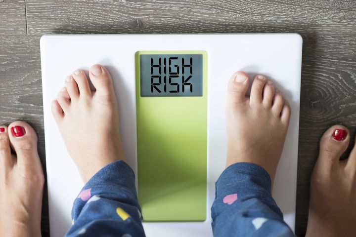 A toddler is standing on a scale with “high risk” written on the display
