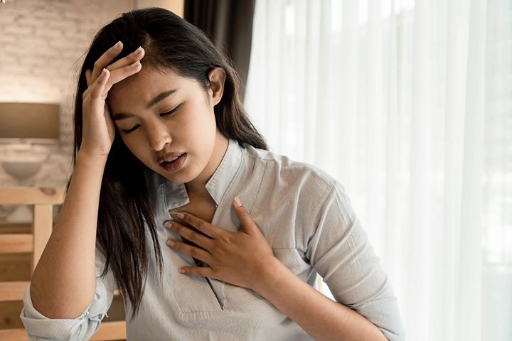Woman holding her chest area with her left hand as she struggles to breathe.