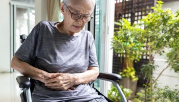 Elderly Asian woman in wheelchair with pain in her abdomen.