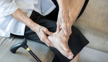 Elderly woman massaging her heel while sitting on a sofa