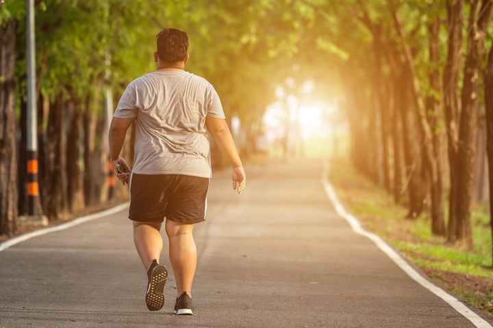 Overweight man in sports attire walking down a road that’s surrounded by trees