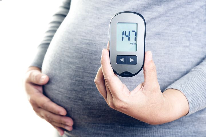 Pregnant woman holding a glucometer with the other hand on her belly