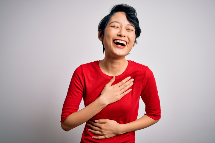 Woman laughing as she places her right hand over her chest and left hand on her abdomen