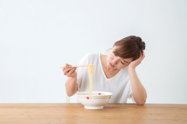 Woman looking at a bowl while she’s holding up noodles with a pair of chopsticks