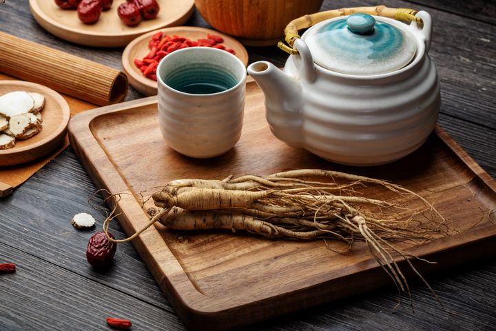 Ginseng root on a tray next to a teapot, a cup of tea and herbs around it