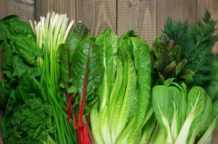 Various types of green leafy vegetables on a wooden surface