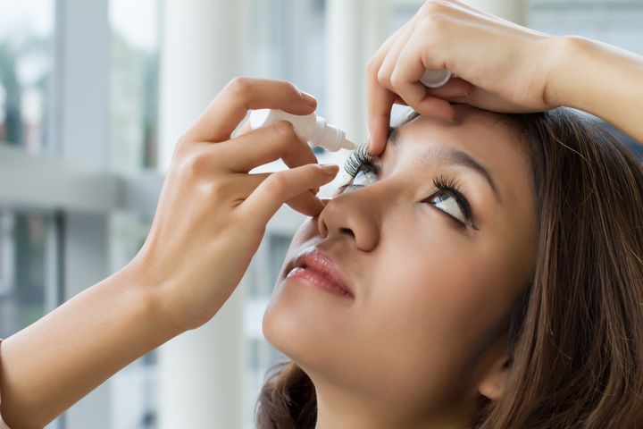 Woman looking up as she applies eye drops to her right eye