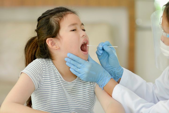 Doctor swabbing a young girl’s throat for testing of throat infection